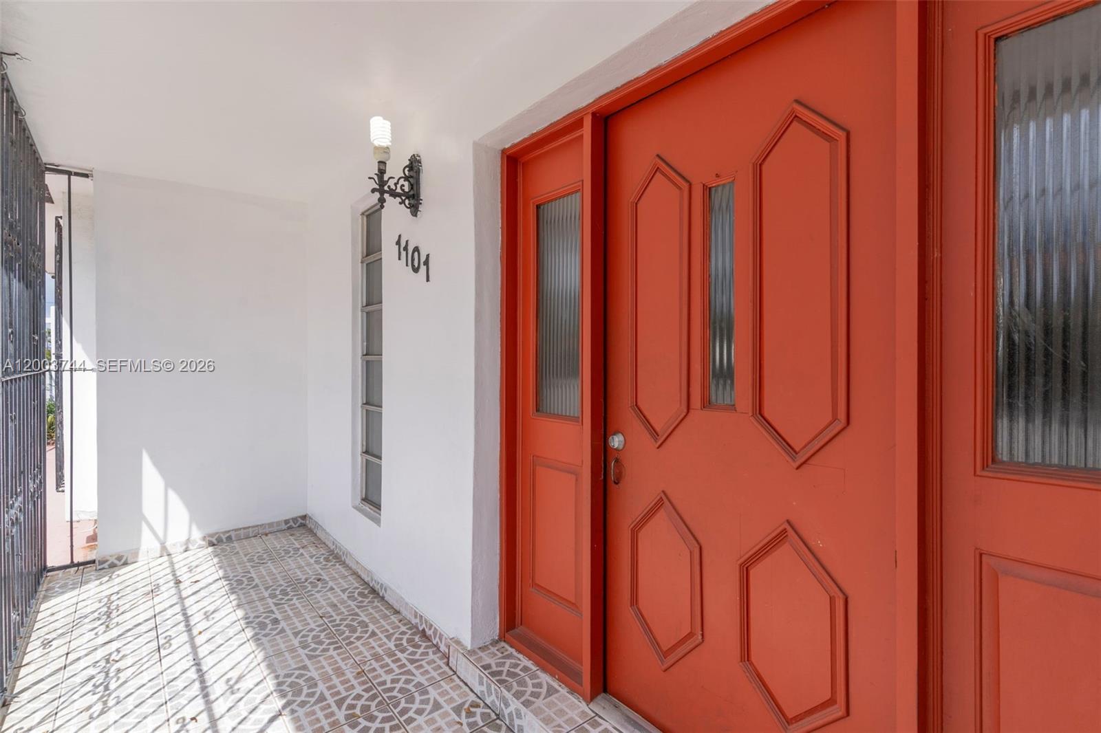 A bright orange front door with glass panels sits beside a white wall with house numbers — 1101 SW 17th Ave # 0, Miami FL 33135, MIAMI, FL