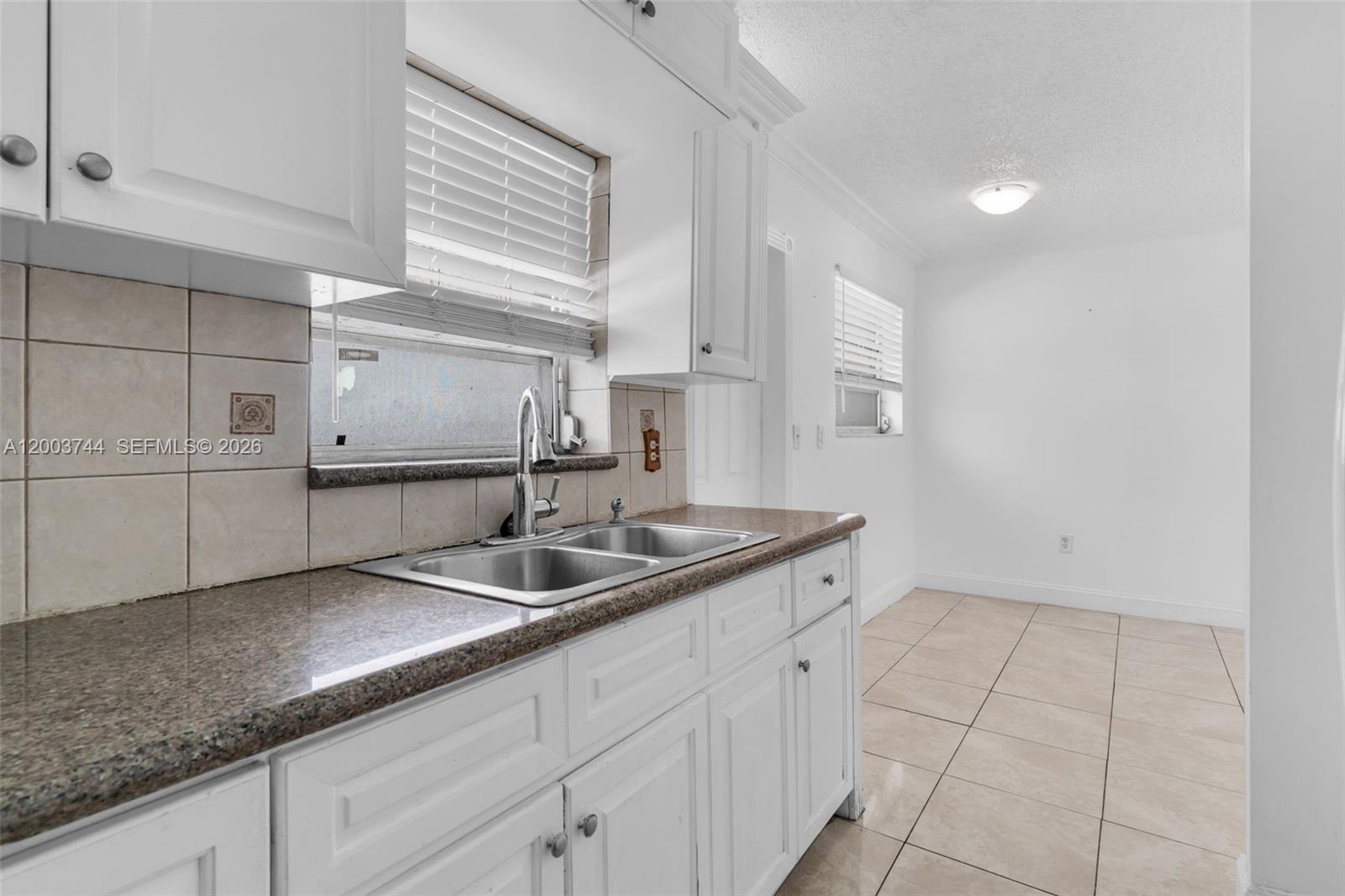A kitchen features white cabinets, granite countertops, a double sink, and light-colored tile flooring — 1101 SW 17th Ave # 0, Miami FL 33135, MIAMI, FL