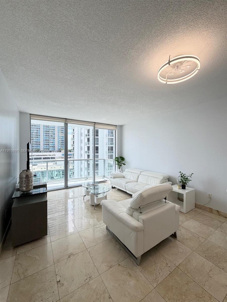A living room with white leather furniture, tile flooring, and a balcony overlooking city buildings — 1050 Brickell Ave # 1904, Miami FL 33131, MIAMI, FL