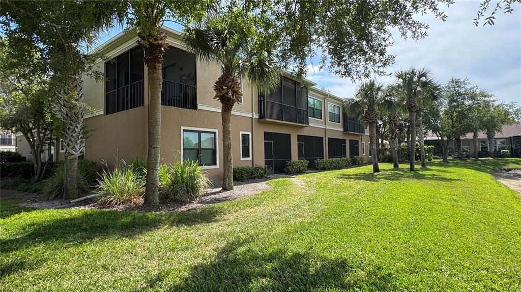 A two-story tan apartment building with screened-in balconies and porches overlooks a grassy lawn — 7338 SKYBIRD ROAD UNIT 413, BRADENTON, FL