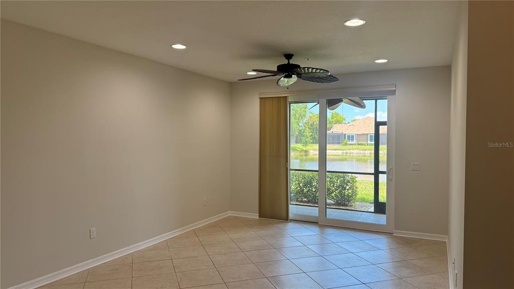 An empty room with tile flooring, a ceiling fan, and sliding doors overlooking a pond — 7338 SKYBIRD ROAD UNIT 413, BRADENTON, FL