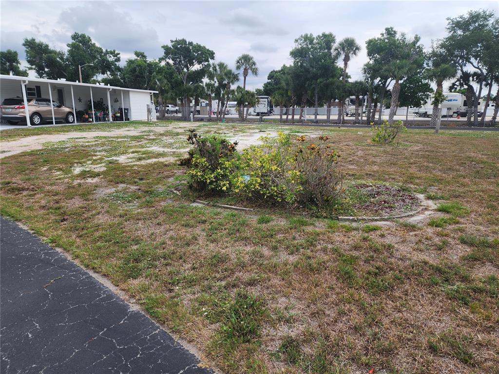 A view of a grassy yard with a central shrub bed and a nearby carport — 5515 DENMARK DRIVE, BRADENTON, FL