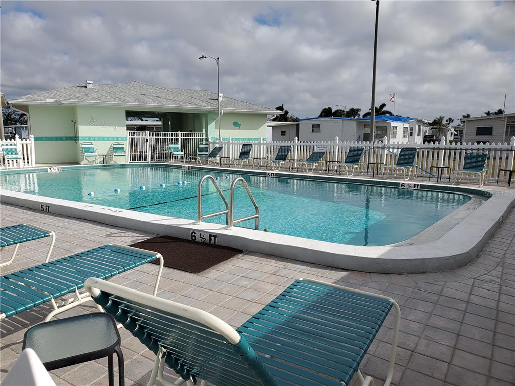 A rectangular swimming pool with lounge chairs sits in front of a light green building — 5515 DENMARK DRIVE, BRADENTON, FL