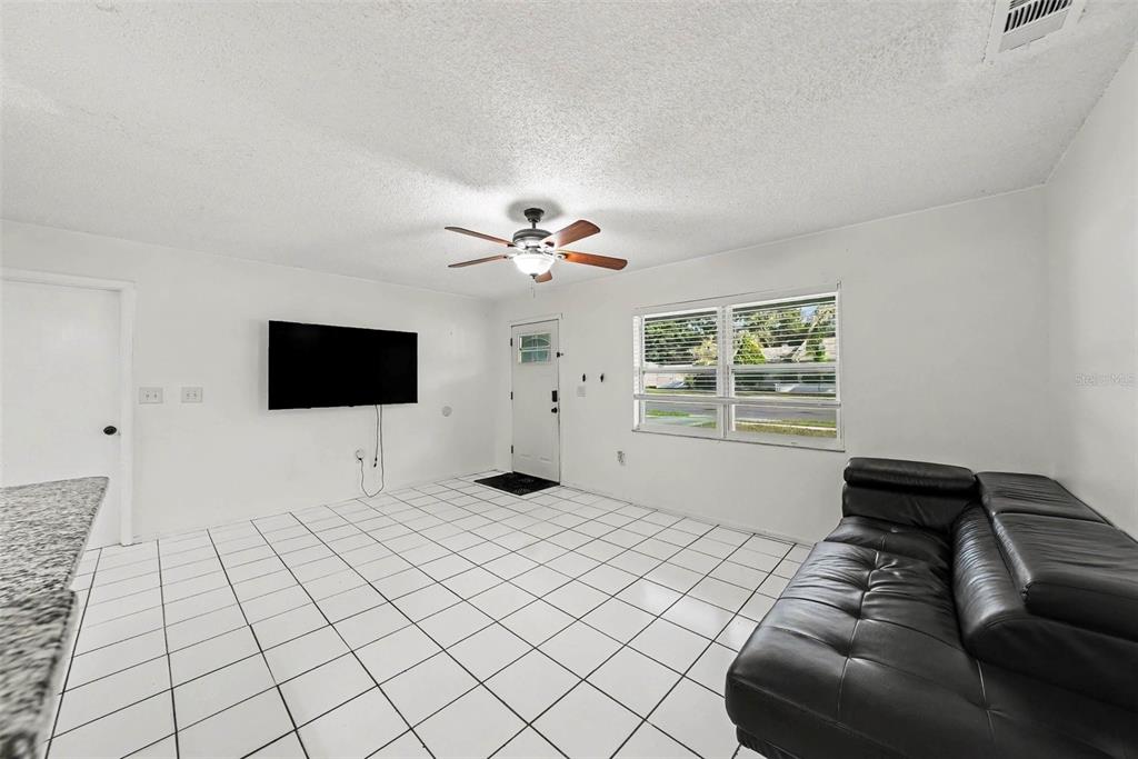 A living room features white tiled floors, a black leather sofa, and a wall-mounted television — 39443 8TH AVENUE, ZEPHYRHILLS, FL