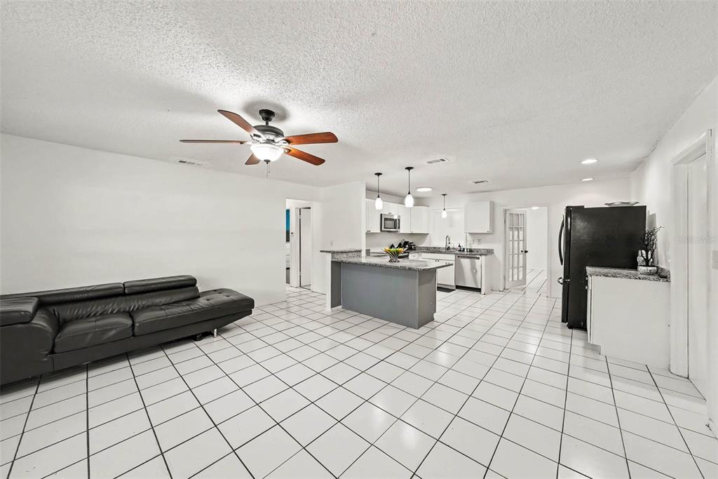 An open-concept living room and kitchen featuring white tile floors, a ceiling fan, and cabinetry — 39443 8TH AVENUE, ZEPHYRHILLS, FL
