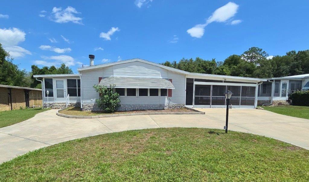 A single-story manufactured home features light gray siding, a screened-in porch, and a concrete driveway — 116 SHER LANE, DEBARY, FL