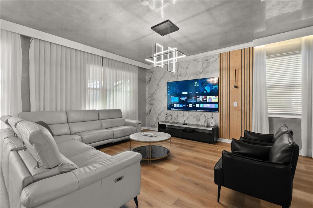 A modern living room features a grey sectional, black armchairs, and a marble-accented media wall — 4324 PROLOGUE WAY, KISSIMMEE, FL