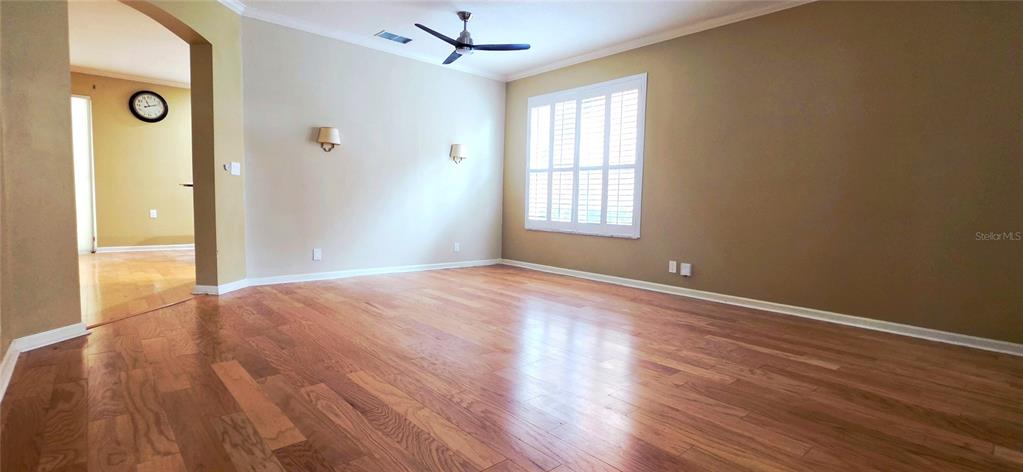 An empty living room features hardwood floors, a ceiling fan, and a window with shutters — 230 W TARRINGTON DRIVE, DELAND, FL