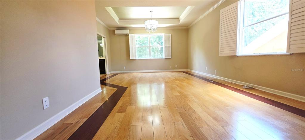 An empty room features light hardwood floors with a dark wood border and a tray ceiling — 230 W TARRINGTON DRIVE, DELAND, FL