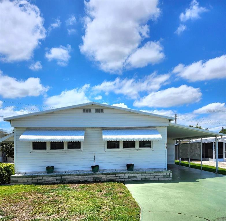 A white single-story manufactured home features a carport, metal awnings, and a brick planter — 6512 TEXAS STREET, BRADENTON, FL