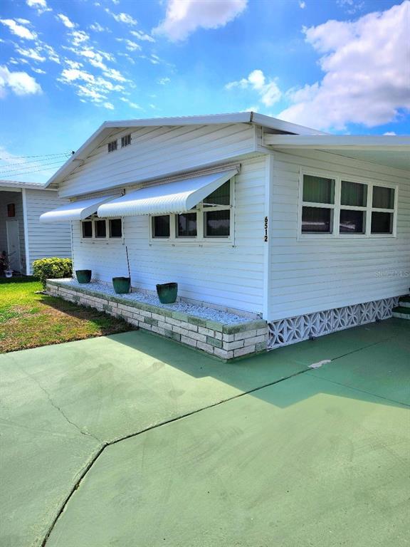 A white mobile home exterior features a green painted driveway, awnings, and a brick planter — 6512 TEXAS STREET, BRADENTON, FL