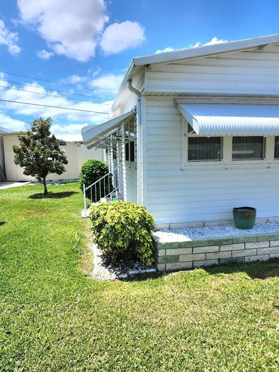 The exterior of a white mobile home features a metal awning and a small bush — 6512 TEXAS STREET, BRADENTON, FL