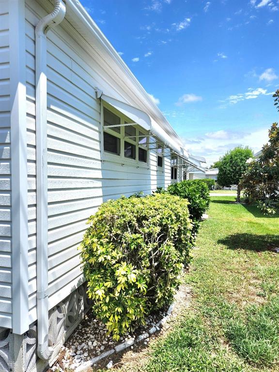The exterior of a white-sided house features metal window awnings and a landscaped bush — 6512 TEXAS STREET, BRADENTON, FL