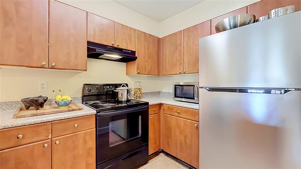 A kitchen features wood cabinets, a black stove, a stainless steel refrigerator, and granite countertops — 202 E SOUTH STREET UNIT 4040, ORLANDO, FL