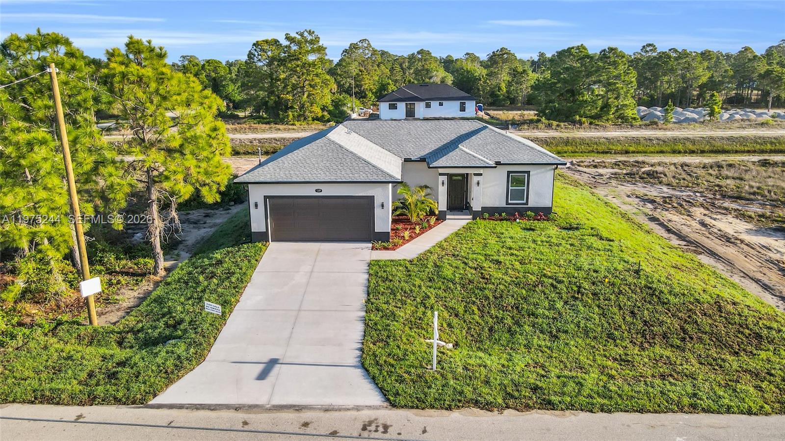 A single-story house with a two-car garage sits on a grassy lot under construction — 1109 EDGEWOOD ST E, Lehigh Acres FL 33974, LEHIGH ACRES, FL