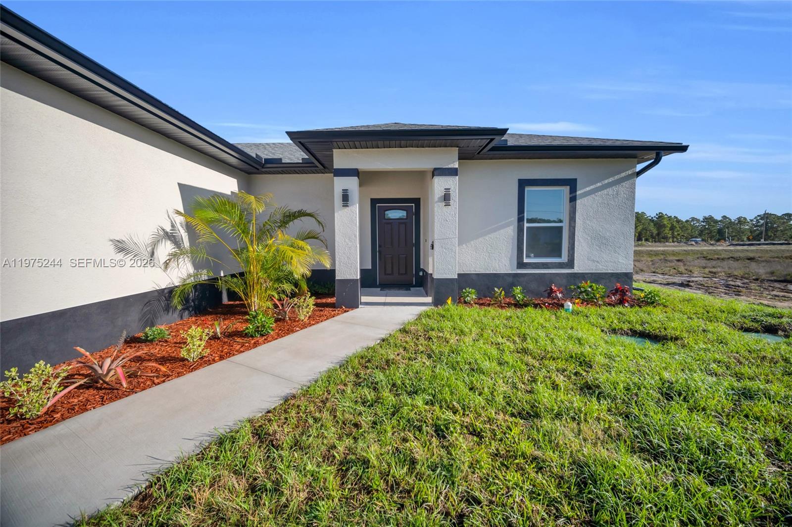 The exterior of a modern house features a concrete walkway leading to a dark front door — 1109 EDGEWOOD ST E, Lehigh Acres FL 33974, LEHIGH ACRES, FL