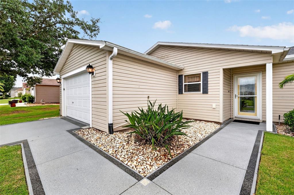 The exterior of a beige, single-story home features a garage, front entrance, and landscaped yard — 1410 RED ASH PLACE, THE VILLAGES, FL