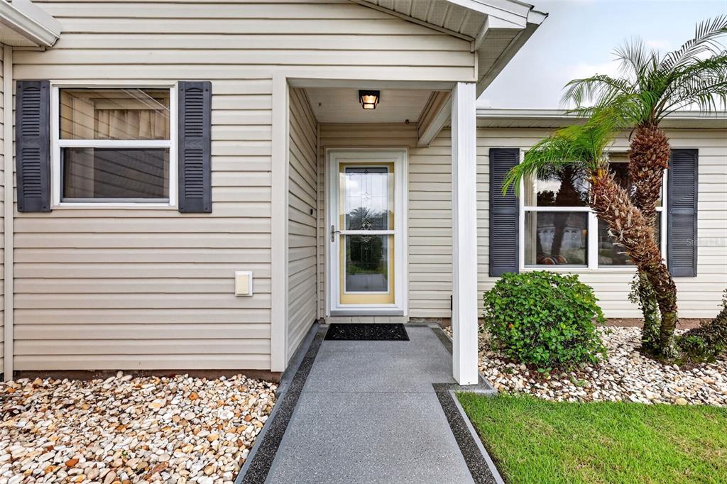 A beige house exterior features a front entrance, a concrete walkway, and a palm tree — 1410 RED ASH PLACE, THE VILLAGES, FL