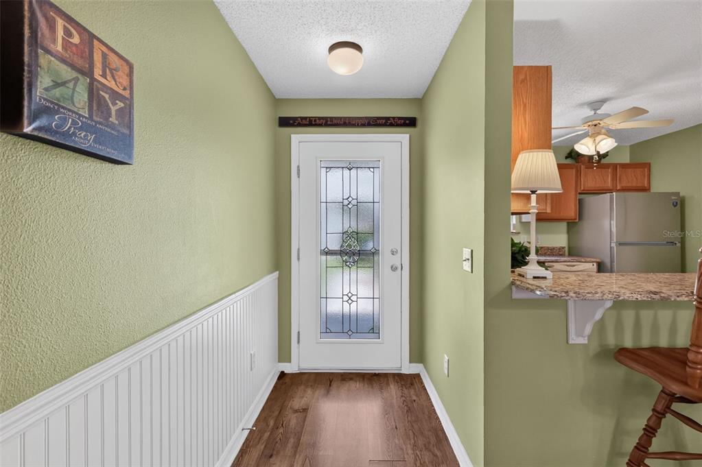 An entryway with green walls, white wainscoting, and wood flooring leads to a front door — 1410 RED ASH PLACE, THE VILLAGES, FL