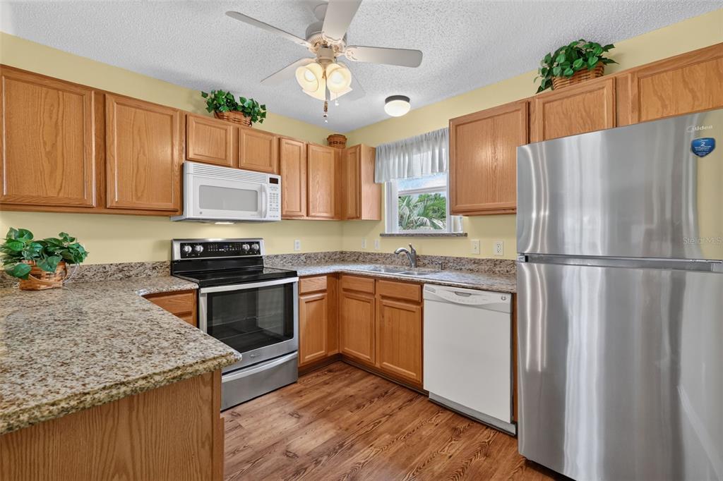 A kitchen with oak cabinets, granite countertops, stainless steel appliances, and wood-look flooring — 1410 RED ASH PLACE, THE VILLAGES, FL