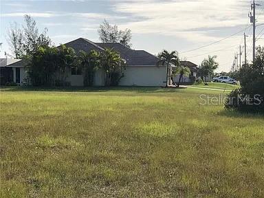 A grassy vacant lot sits in front of a single-story suburban house with palm trees — 339 NE 19TH TERRACE, CAPE CORAL, FL