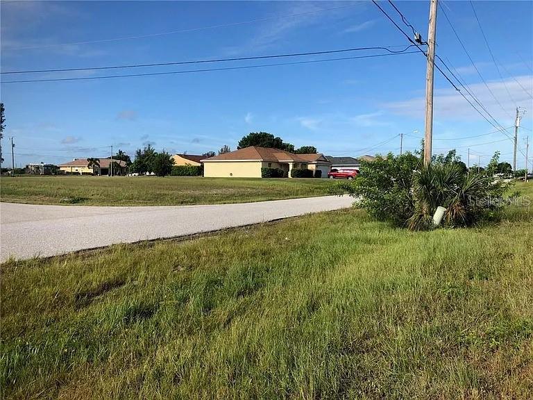 A grassy vacant lot sits beside a paved road with residential houses in the background — 339 NE 19TH TERRACE, CAPE CORAL, FL