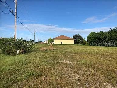 A grassy vacant lot sits in front of a single-story house under a blue sky — 339 NE 19TH TERRACE, CAPE CORAL, FL