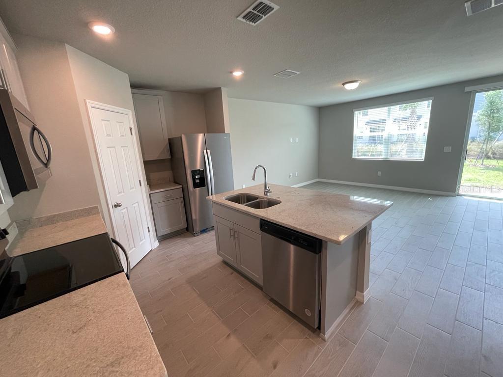 A kitchen with a granite-topped island, stainless steel appliances, and light-colored tile flooring — 513 LEGACY LOOP, DAVENPORT, FL