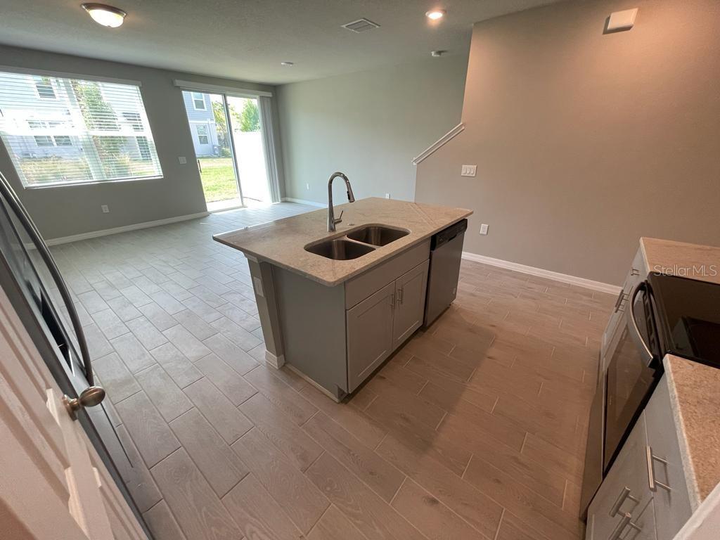 A kitchen with a central island, stainless steel sink, and light-colored tile flooring — 513 LEGACY LOOP, DAVENPORT, FL