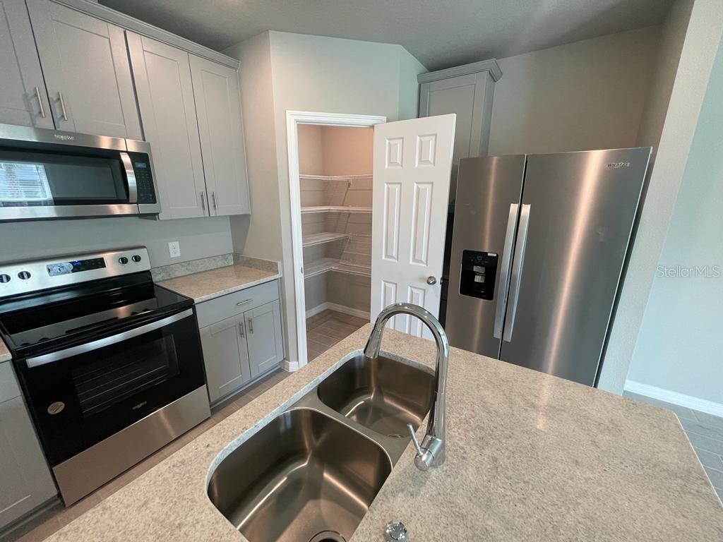 A kitchen features gray cabinets, stainless steel appliances, a center island sink, and a pantry — 513 LEGACY LOOP, DAVENPORT, FL