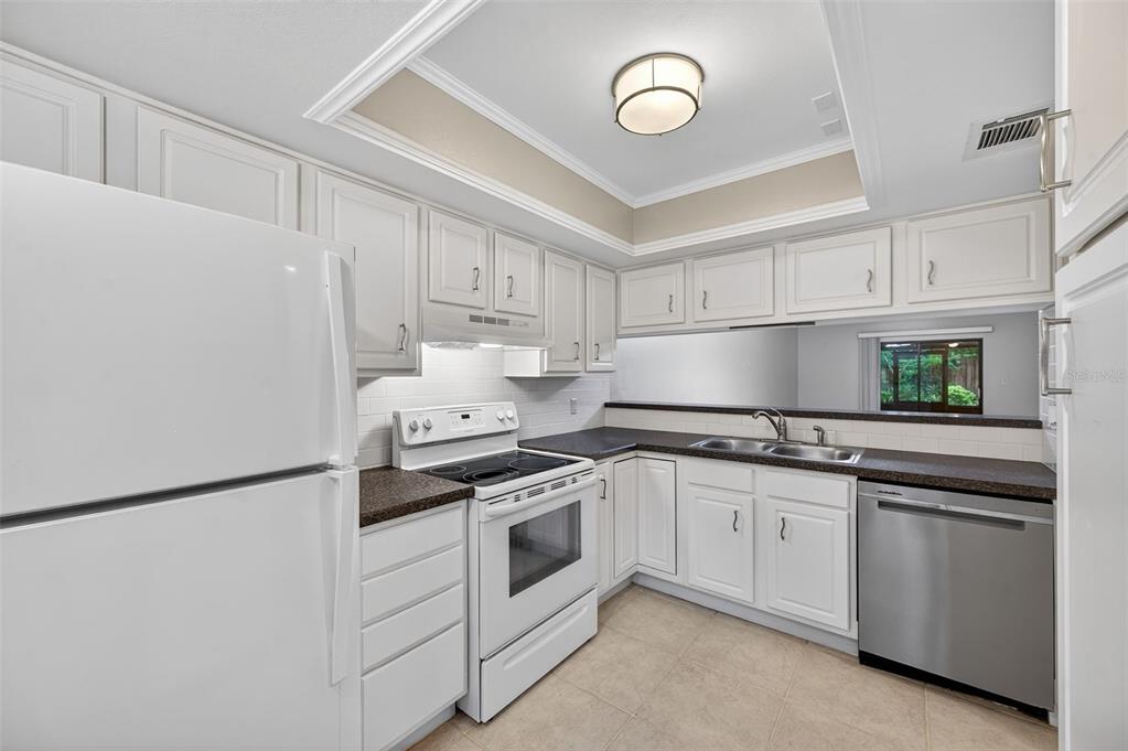 A kitchen with white cabinets, dark countertops, white appliances, and a stainless steel dishwasher — 39650 US HIGHWAY 19 N UNIT 565, TARPON SPRINGS, FL