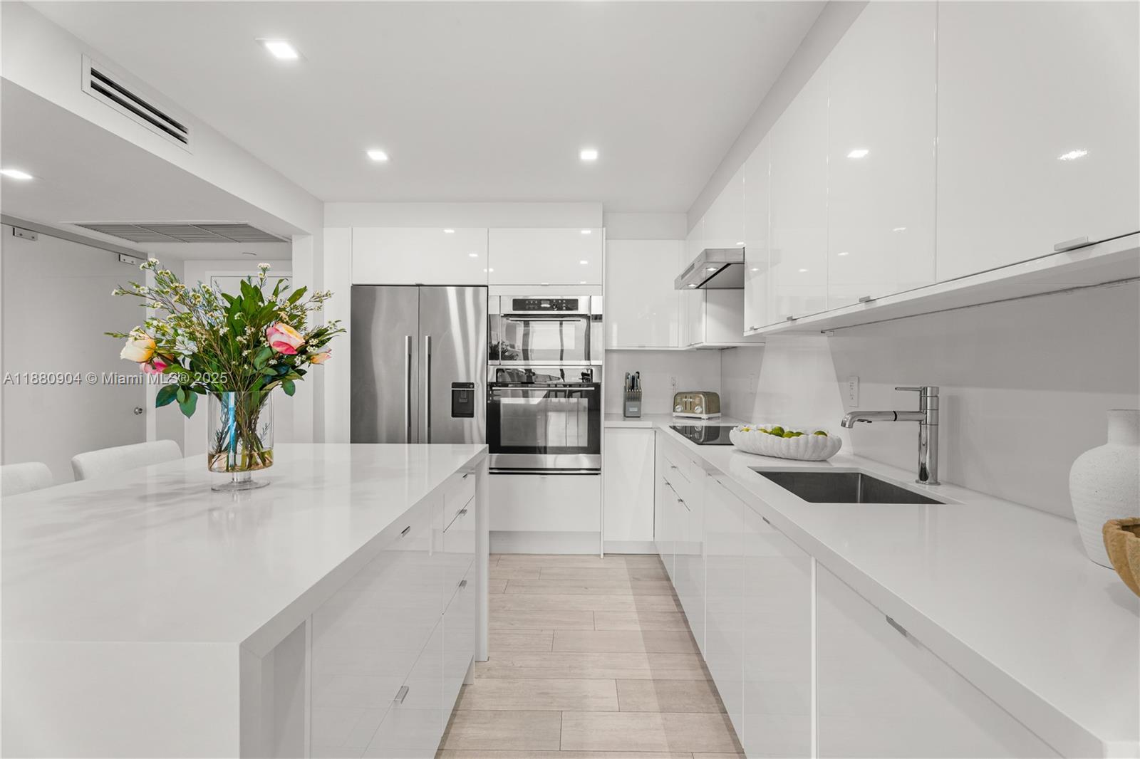 A modern white kitchen features a central island, stainless steel appliances, and light wood flooring — 2301 Collins Ave # 24, Miami Beach FL 33139, MIAMI BEACH, FL