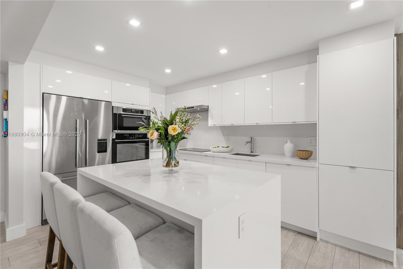 A modern kitchen features white glossy cabinets, a central island, and stainless steel appliances — 2301 Collins Ave # 24, Miami Beach FL 33139, MIAMI BEACH, FL