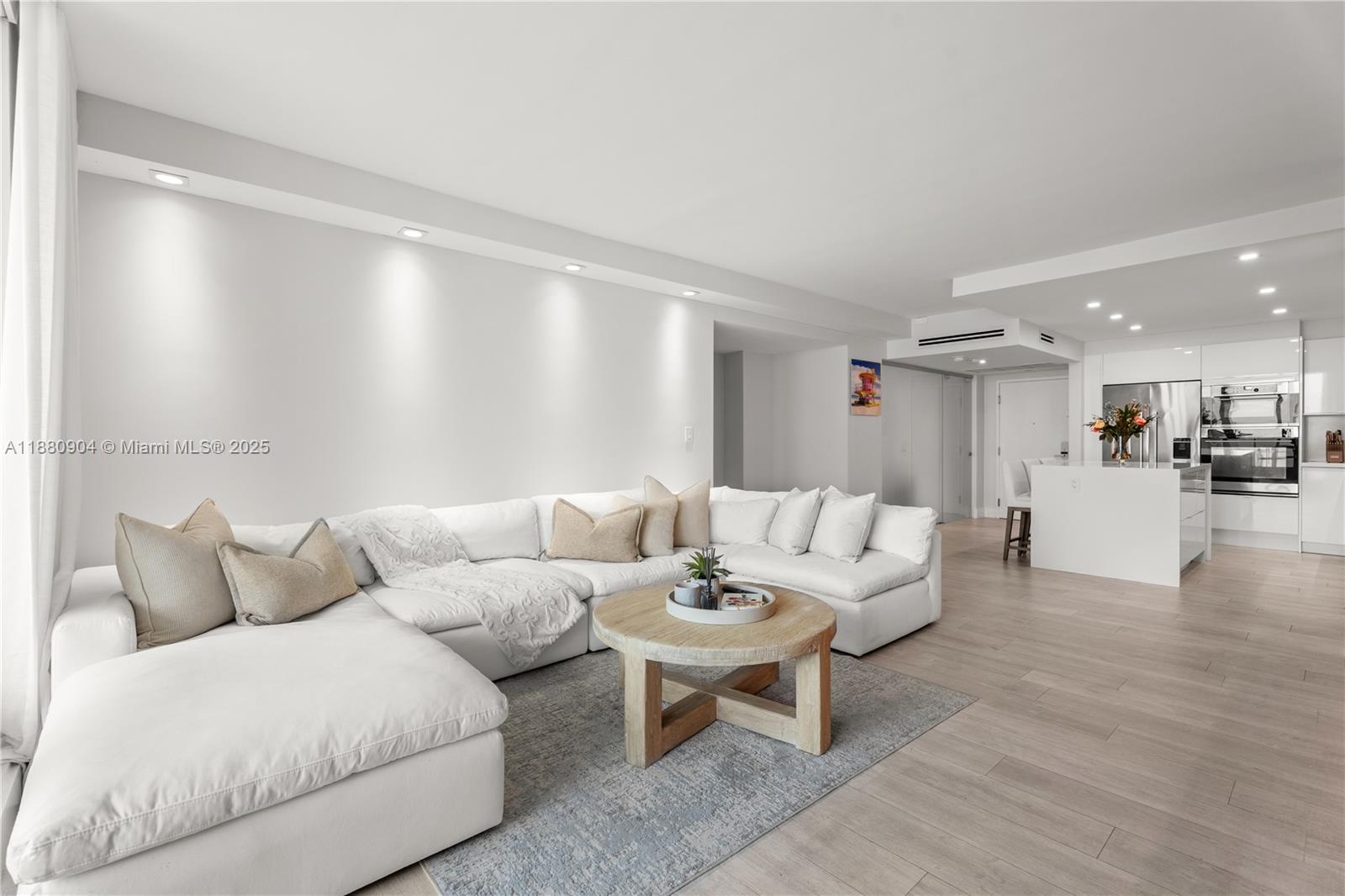 A modern living room features a large white sectional sofa, a wooden coffee table, and kitchen — 2301 Collins Ave # 24, Miami Beach FL 33139, MIAMI BEACH, FL