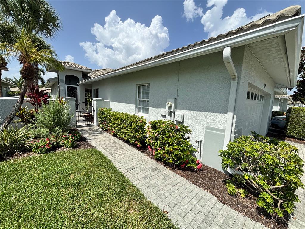 A paved walkway leads to a gated courtyard entrance beside a light-colored stucco house — 310 RECLINATA CIRCLE, VENICE, FL