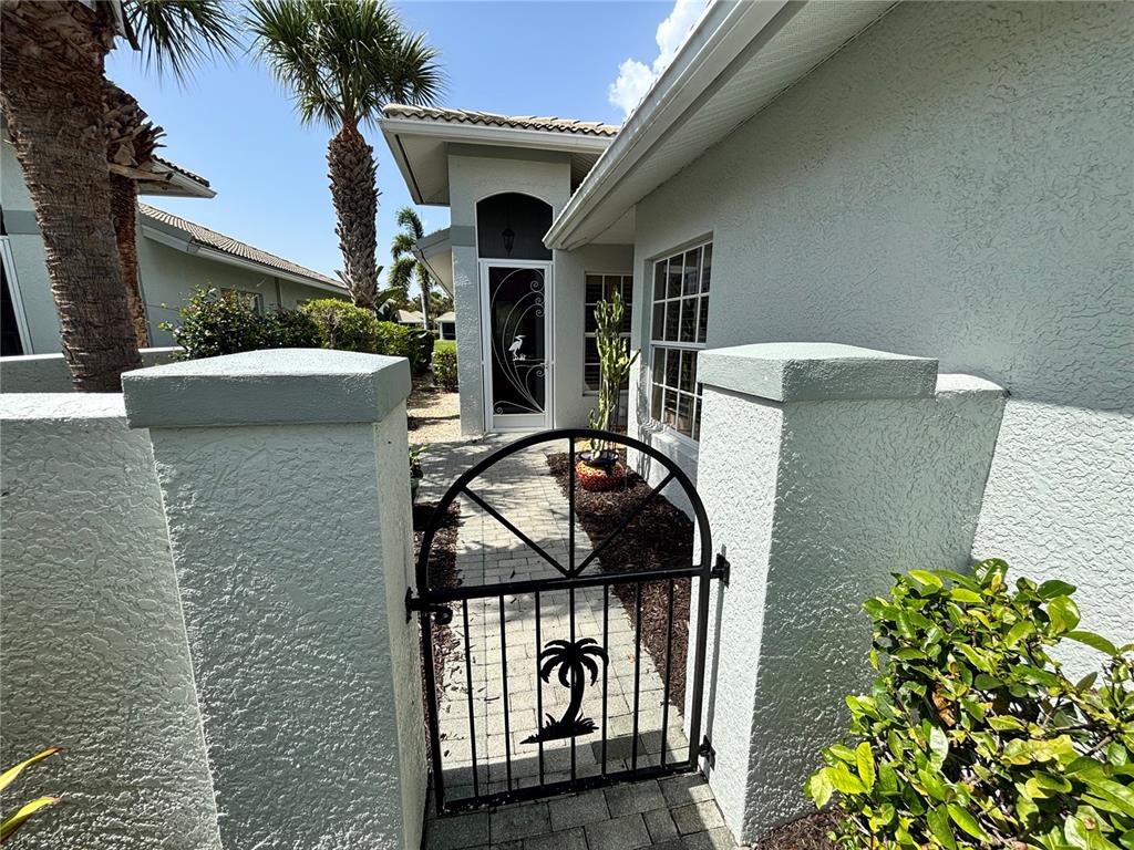 A metal gate with a palm tree design leads to a paved walkway and entryway — 310 RECLINATA CIRCLE, VENICE, FL
