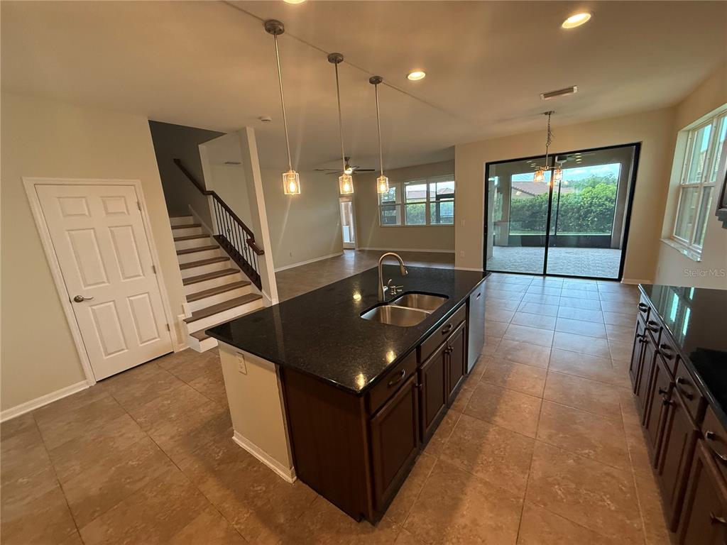 A kitchen with a dark granite island, brown cabinets, and tile flooring overlooks a living area — 3969 AQUILLA DRIVE, LAKELAND, FL