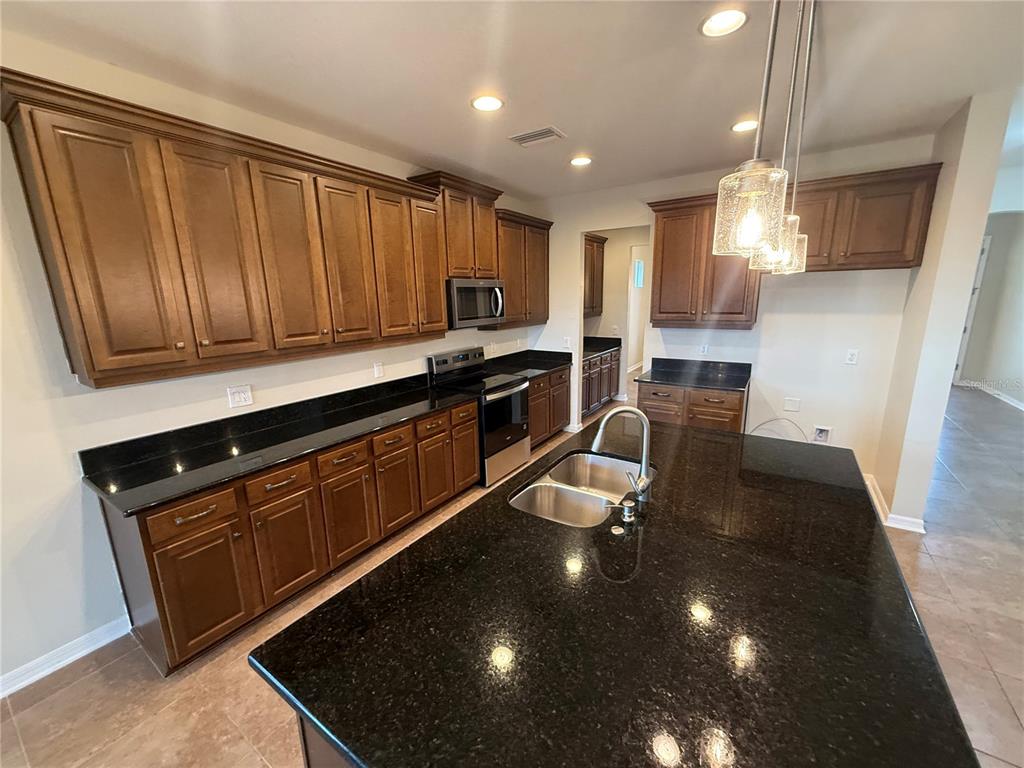 A kitchen features dark wood cabinets, black granite countertops, a large island, and stainless appliances — 3969 AQUILLA DRIVE, LAKELAND, FL