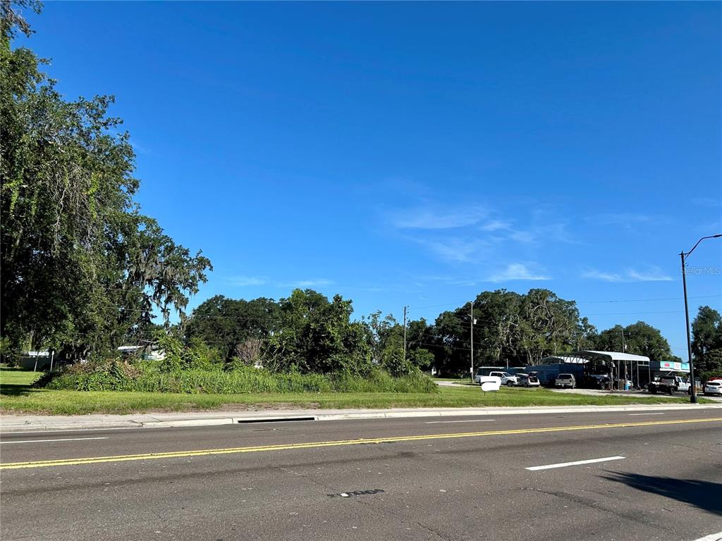A vacant, grassy lot sits beside a road with trees and a nearby covered structure — 109 ORANGE STREET, BOWLING GREEN, FL