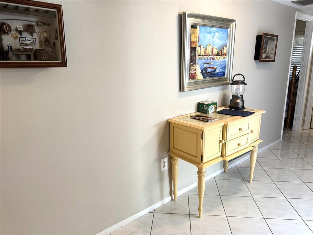 A hallway features a yellow wooden console table, wall art, and light-colored tile flooring — 2571 RIVERBLUFF PARKWAY UNIT V158, SARASOTA, FL