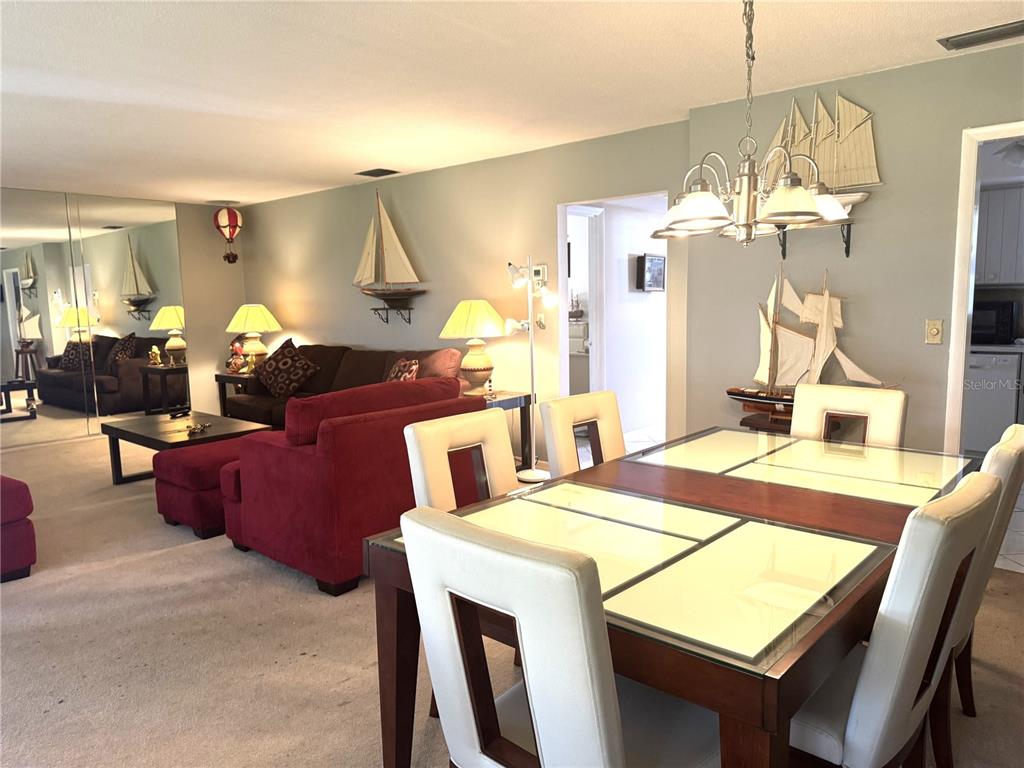 A dining area with a glass-topped table and chairs sits beside a living room — 2571 RIVERBLUFF PARKWAY UNIT V158, SARASOTA, FL