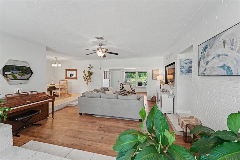 A living room features a piano, a gray sofa, wood flooring, and a white brick wall — 8879 LAKEWOOD DRIVE, SEMINOLE, FL