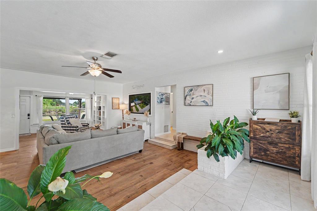 A living room features white brick walls, wood flooring, a ceiling fan, and a sectional sofa — 8879 LAKEWOOD DRIVE, SEMINOLE, FL