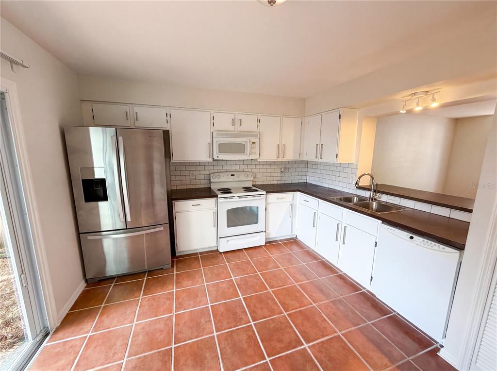 A kitchen features white cabinets, stainless steel appliances, dark countertops, and terracotta floor tiles — 510 GREEN SPRING CIRCLE, WINTER SPRINGS, FL