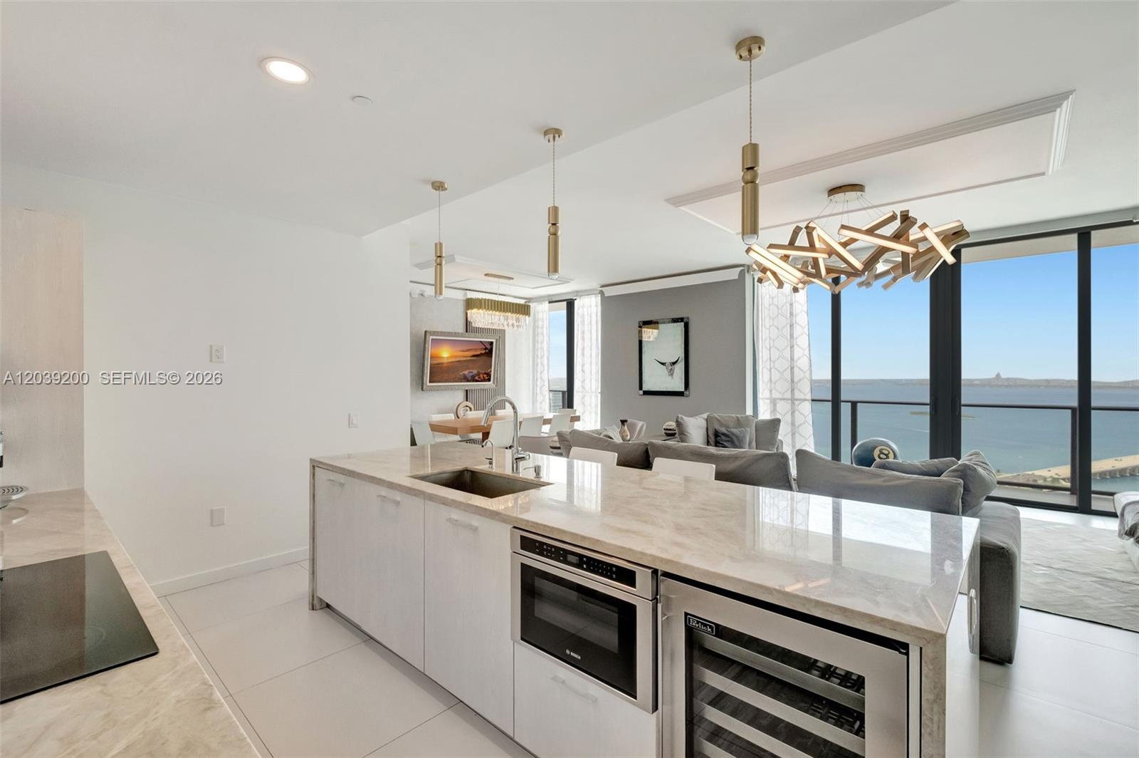 A modern kitchen island with a built-in microwave and wine cooler overlooks a living area — 501 NE 31st St, Miami FL 33137, MIAMI, FL
