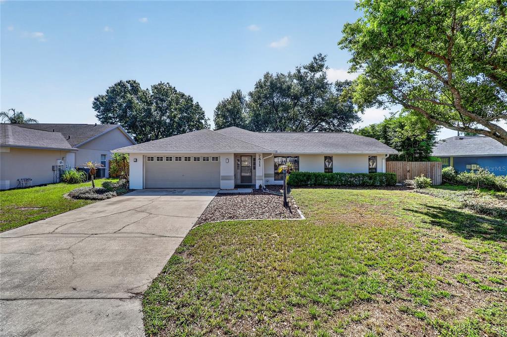 A single-story house with a two-car garage, light-colored siding, and a concrete driveway — 7411 FLORAL CIRCLE E, LAKELAND, FL