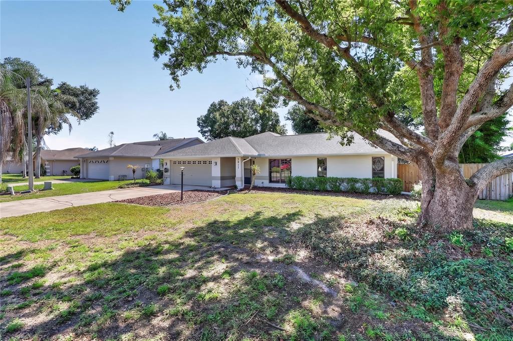 A single-story house with a beige exterior, a two-car garage, and a large front tree — 7411 FLORAL CIRCLE E, LAKELAND, FL