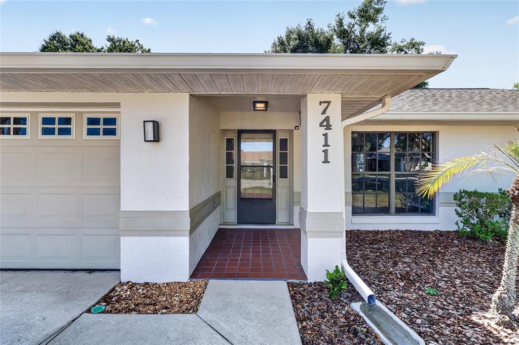 The exterior of a single-story home features a garage, a covered entryway, and house numbers — 7411 FLORAL CIRCLE E, LAKELAND, FL