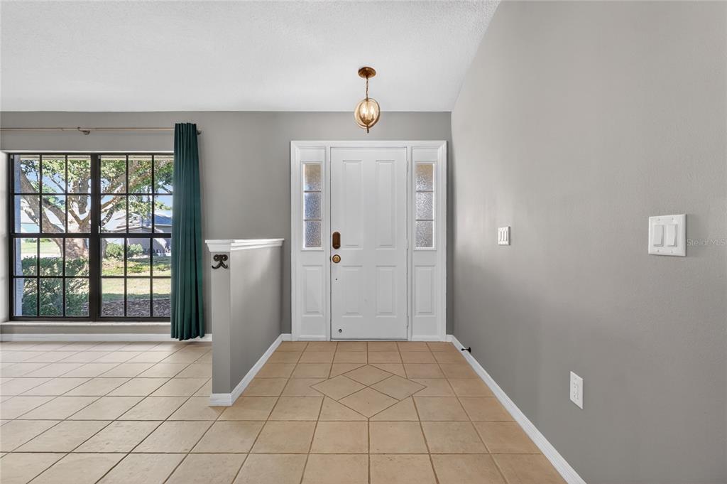 An entryway features light-colored tile flooring, a white front door, and gray walls — 7411 FLORAL CIRCLE E, LAKELAND, FL