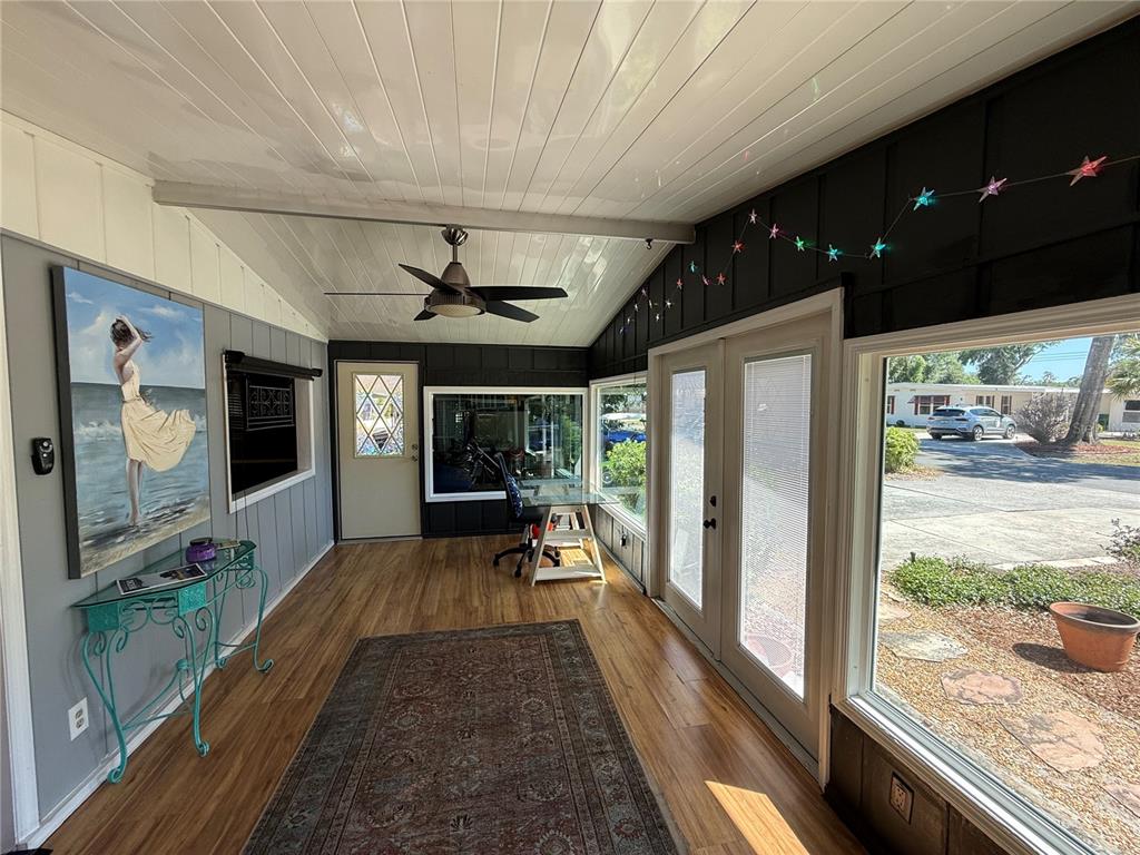 A sunroom features wood-look flooring, a ceiling fan, a large painting, and glass exterior doors — 9 S BOBWHITE ROAD, WILDWOOD, FL
